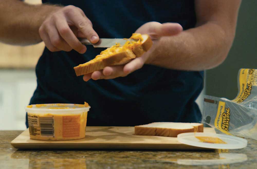 man in kitchen spreading pimento cheese on sliced bread